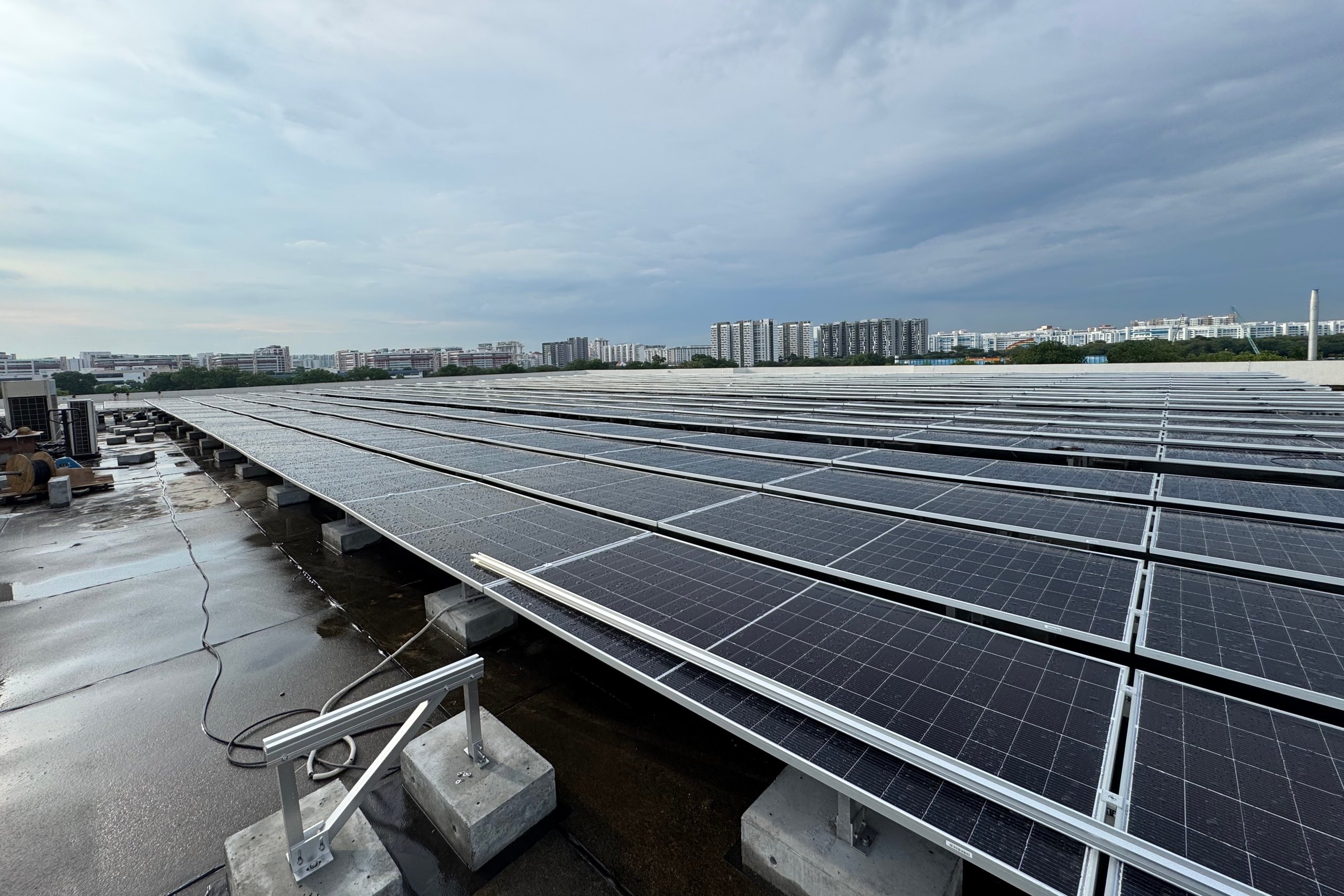 Rows of solar panels on ballasted frames across a flat factory roof in Defu, housing blocks on the skyline