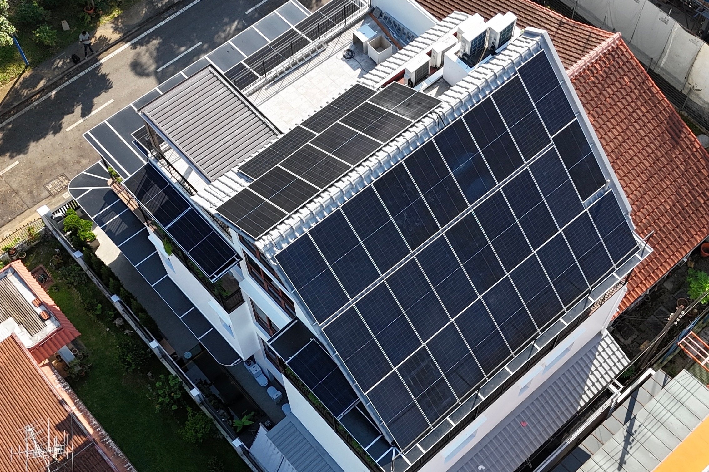 Angled drone view of the Kranji house, its long pitched roof and upper terrace covered in solar panels