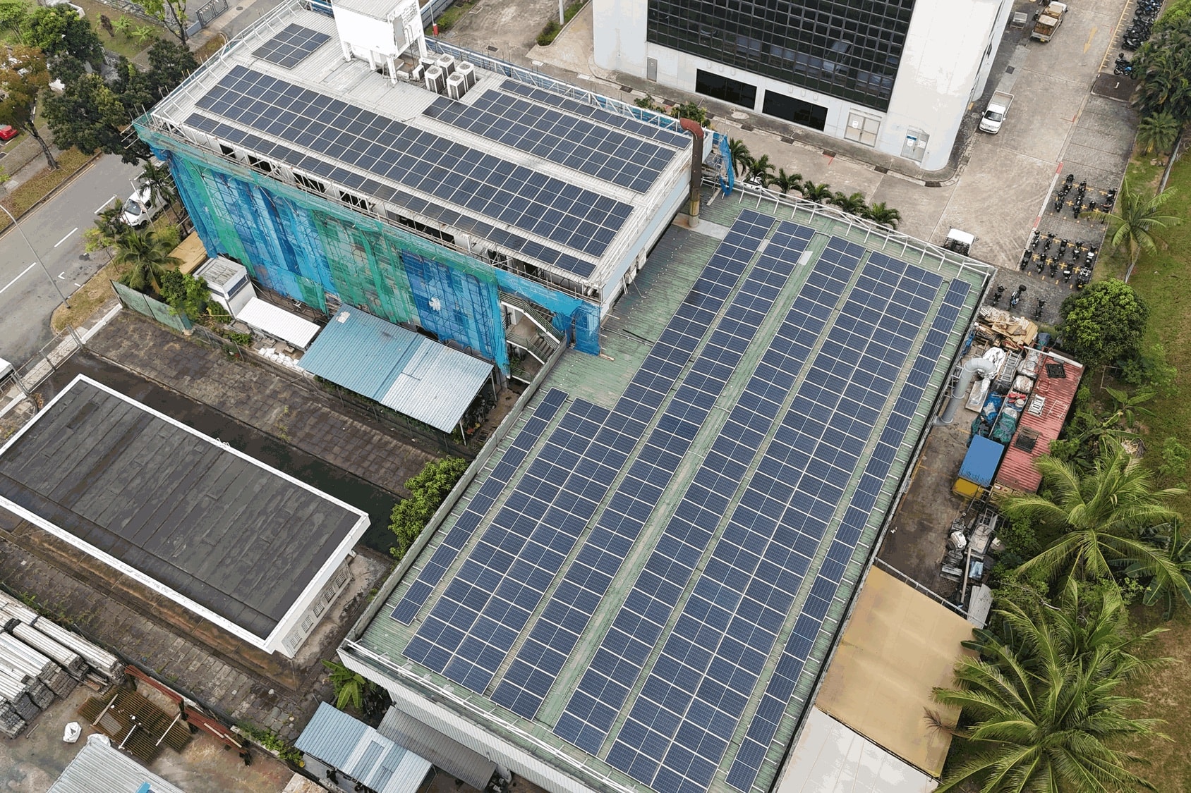 Drone view of the Joo Koon factory, rows of solar panels across its long green metal roof and more on the taller block beside it